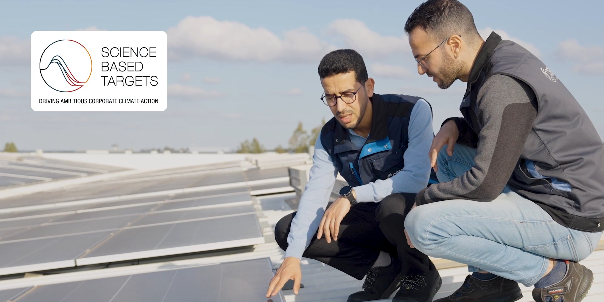 Two colleagues reviewing solar panels on a rooftop, with the Science Based Targets logo