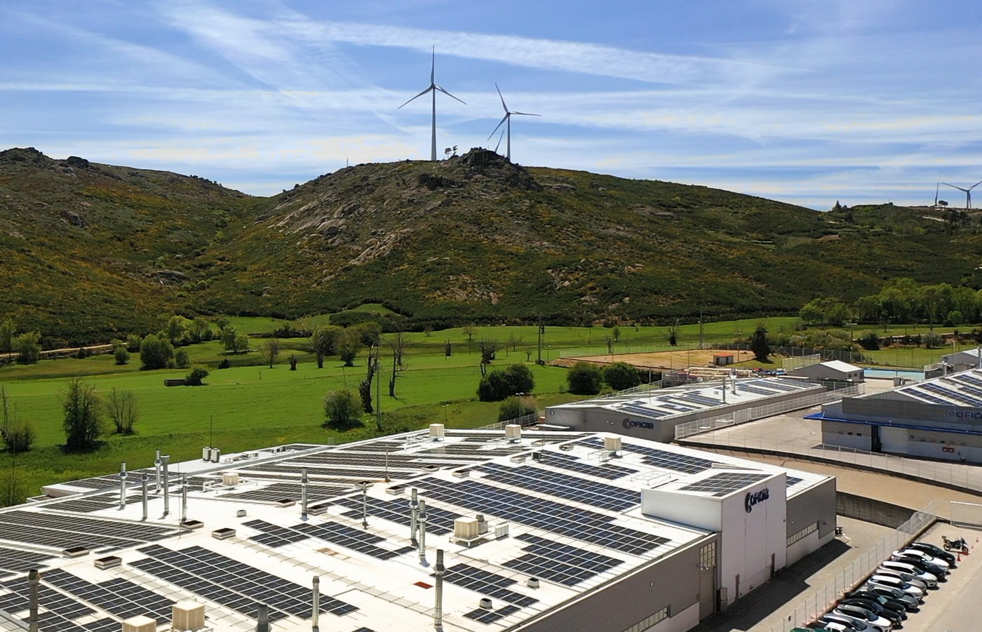 COFICAB plant with rooftop solar panels and wind turbines on the hill behind